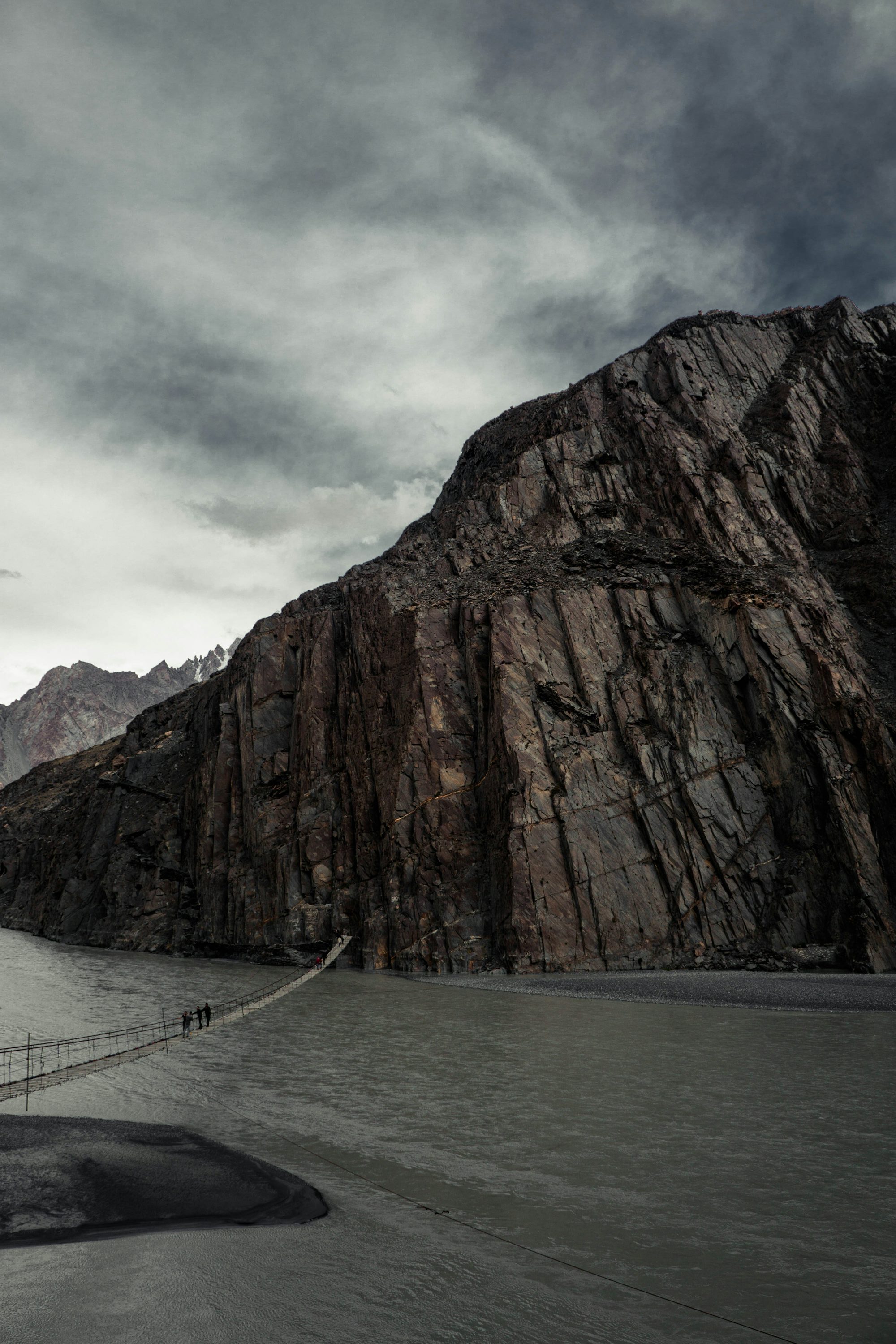 bridge above water towers rock mountain under cloudy sky